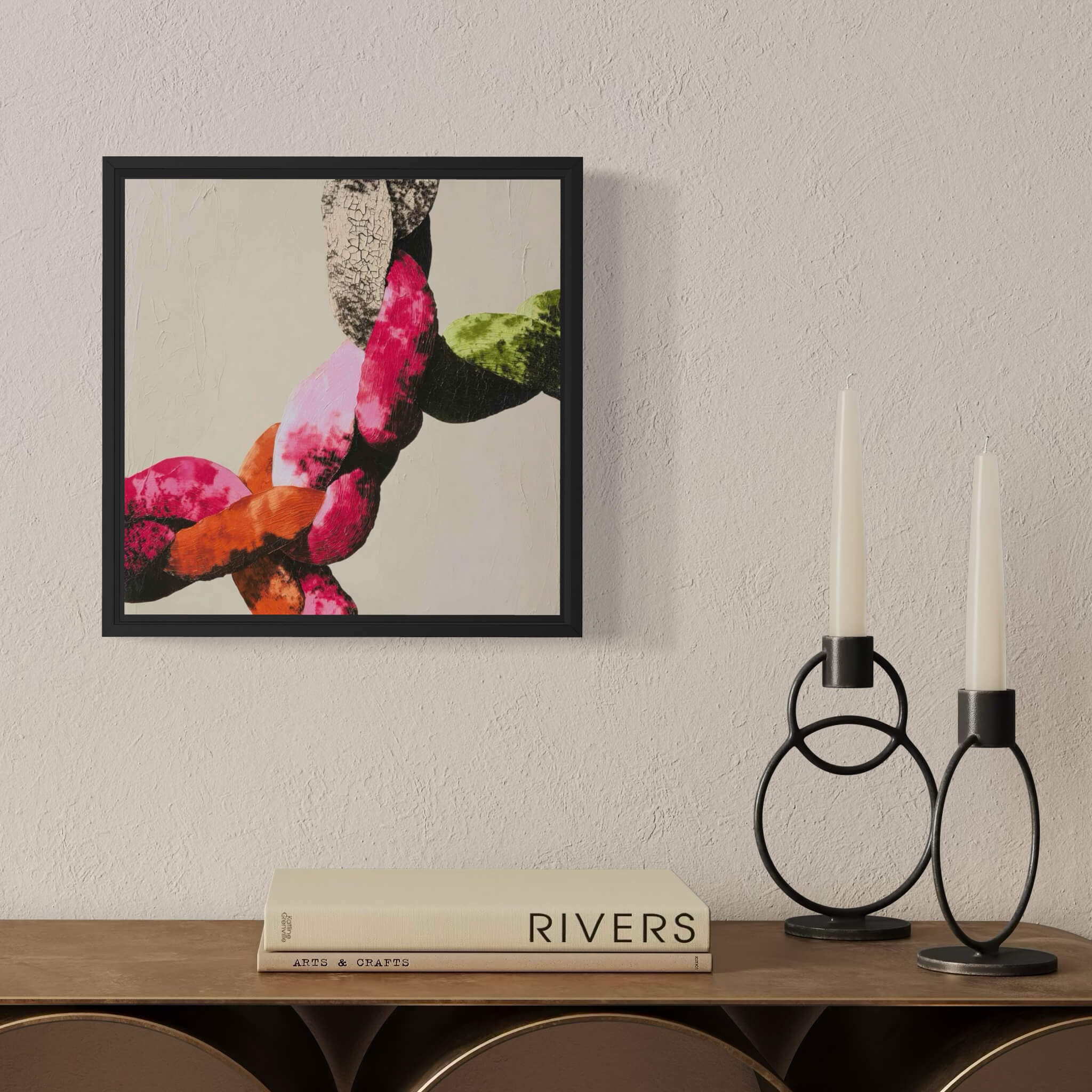 Framed abstract art on a wall above a wooden shelf with books and candle holders.