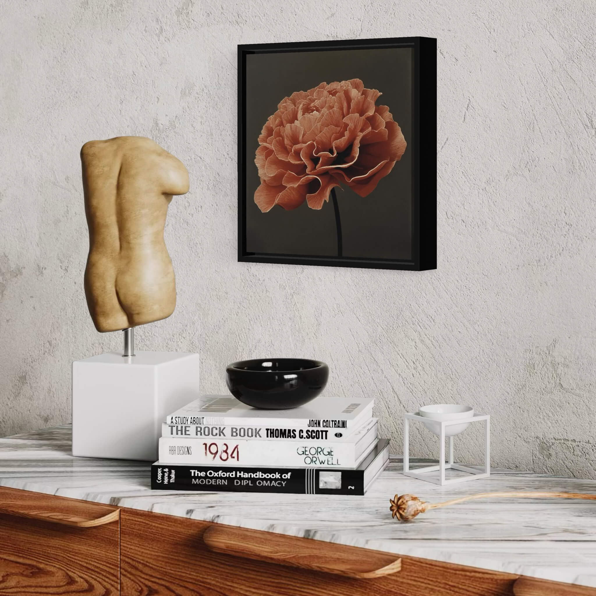 Decorative setup with a framed flower fine art print, statue, books, and bowl on a table against a textured wall.