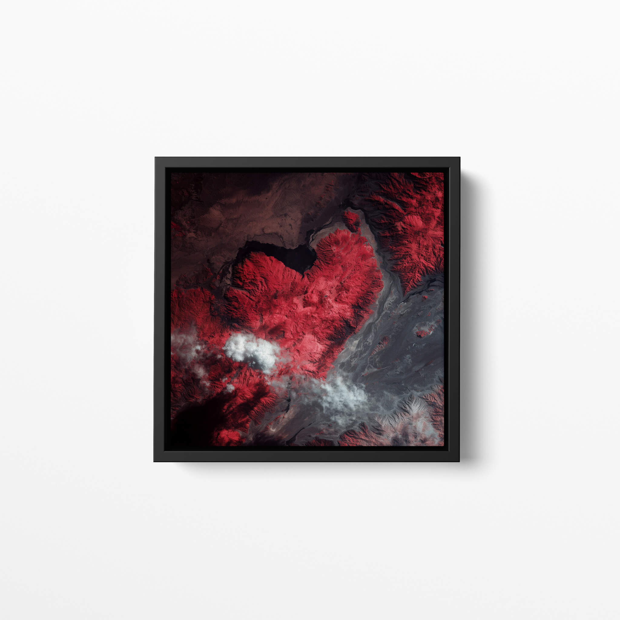 Framed artwork of an infrared satellite photography of a mountain shaped like a heart on a white wall
