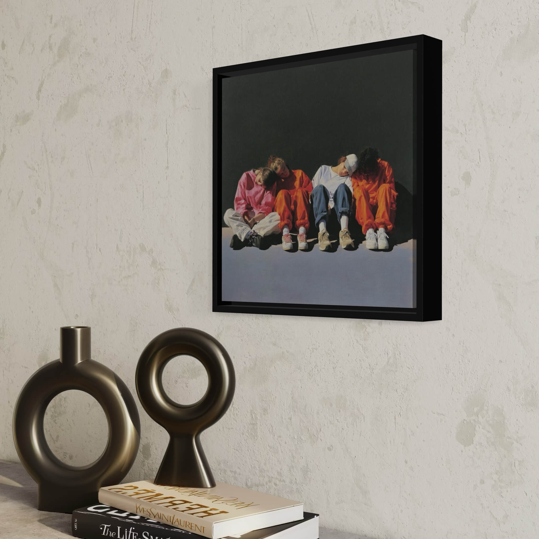 Framed artwork of four people sitting on a wall with decorative vases and books below.