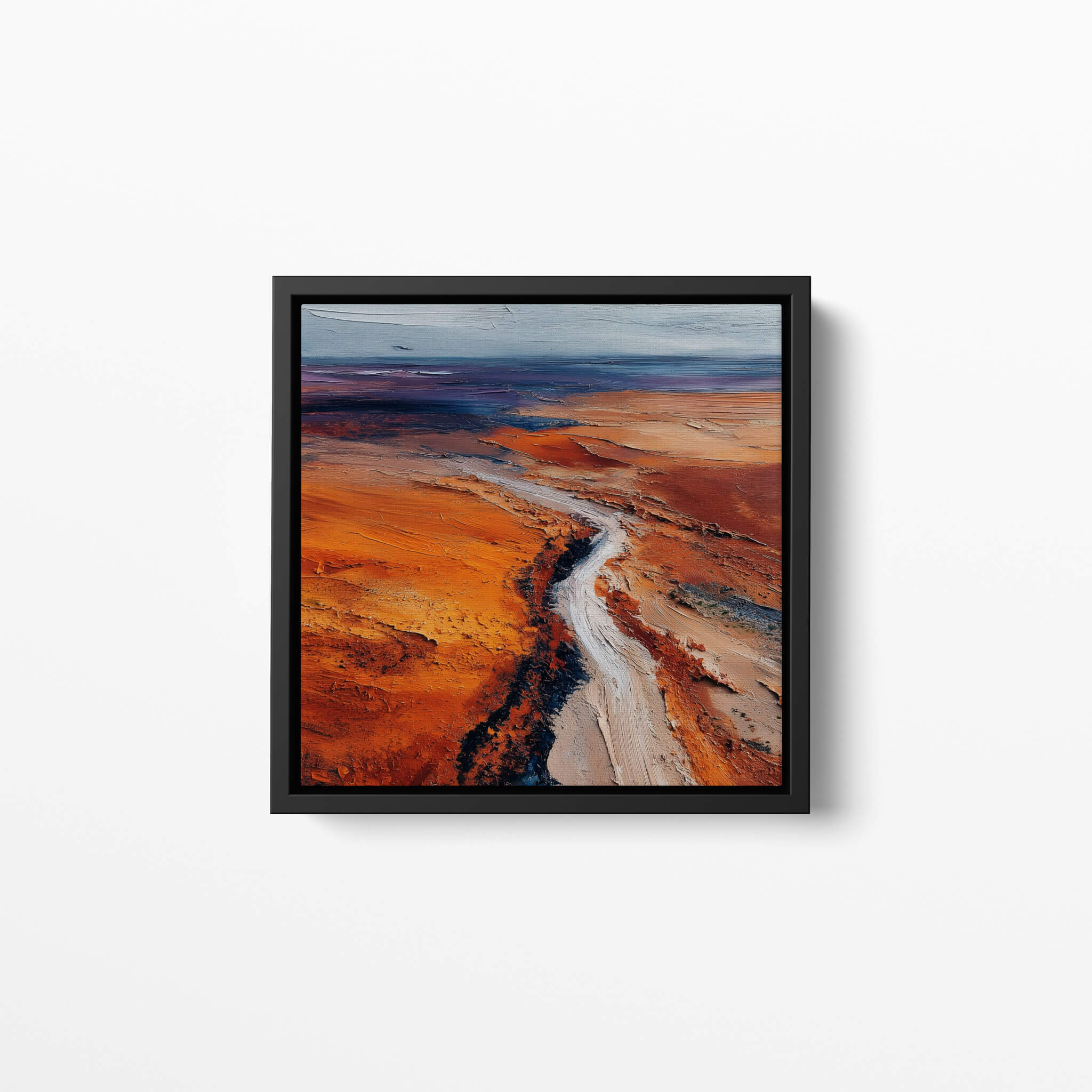 Framed oil paints artwork of a desert landscape with a winding road on a white wall.