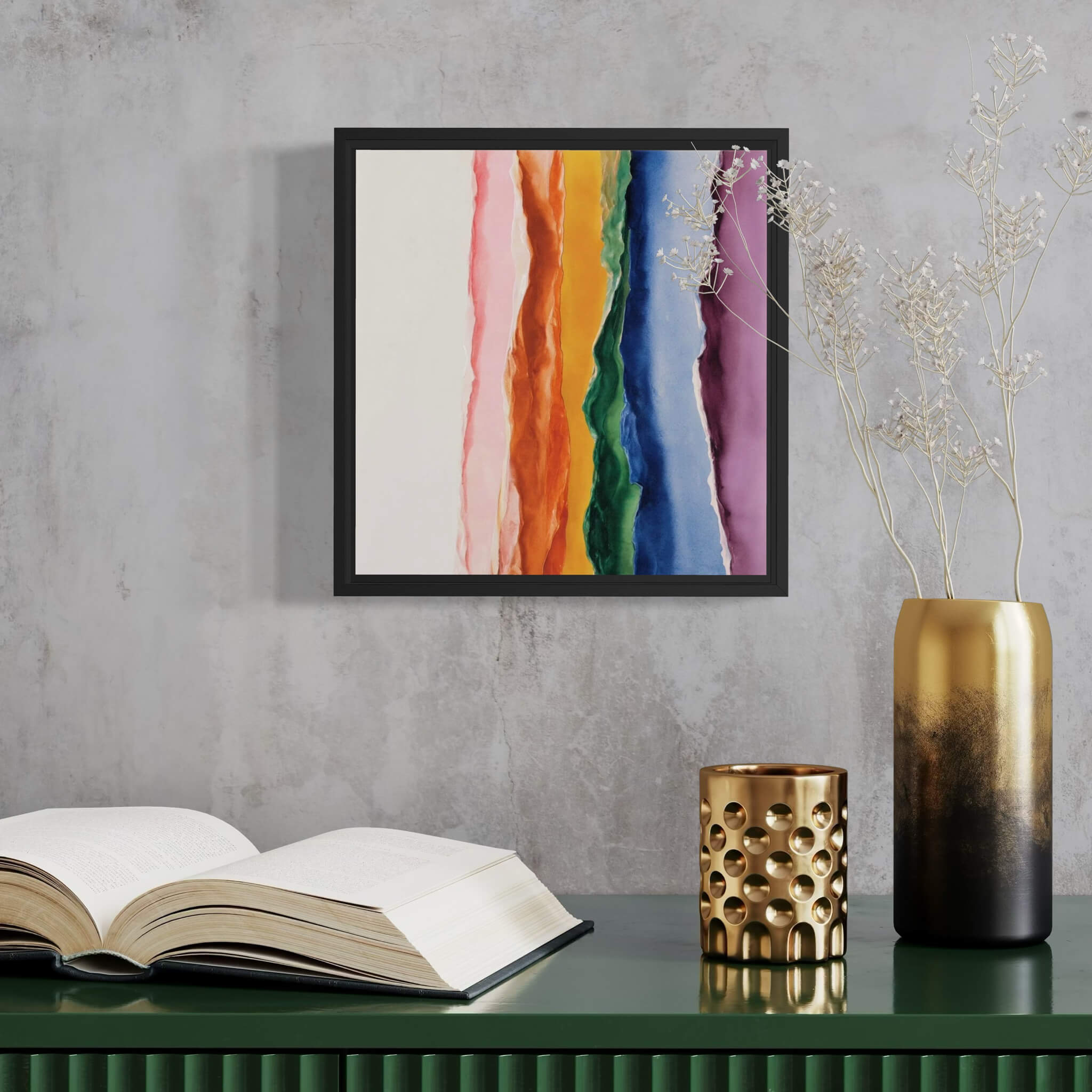 Framed abstract artwork with a book and decorative vase on a table against a gray wall.