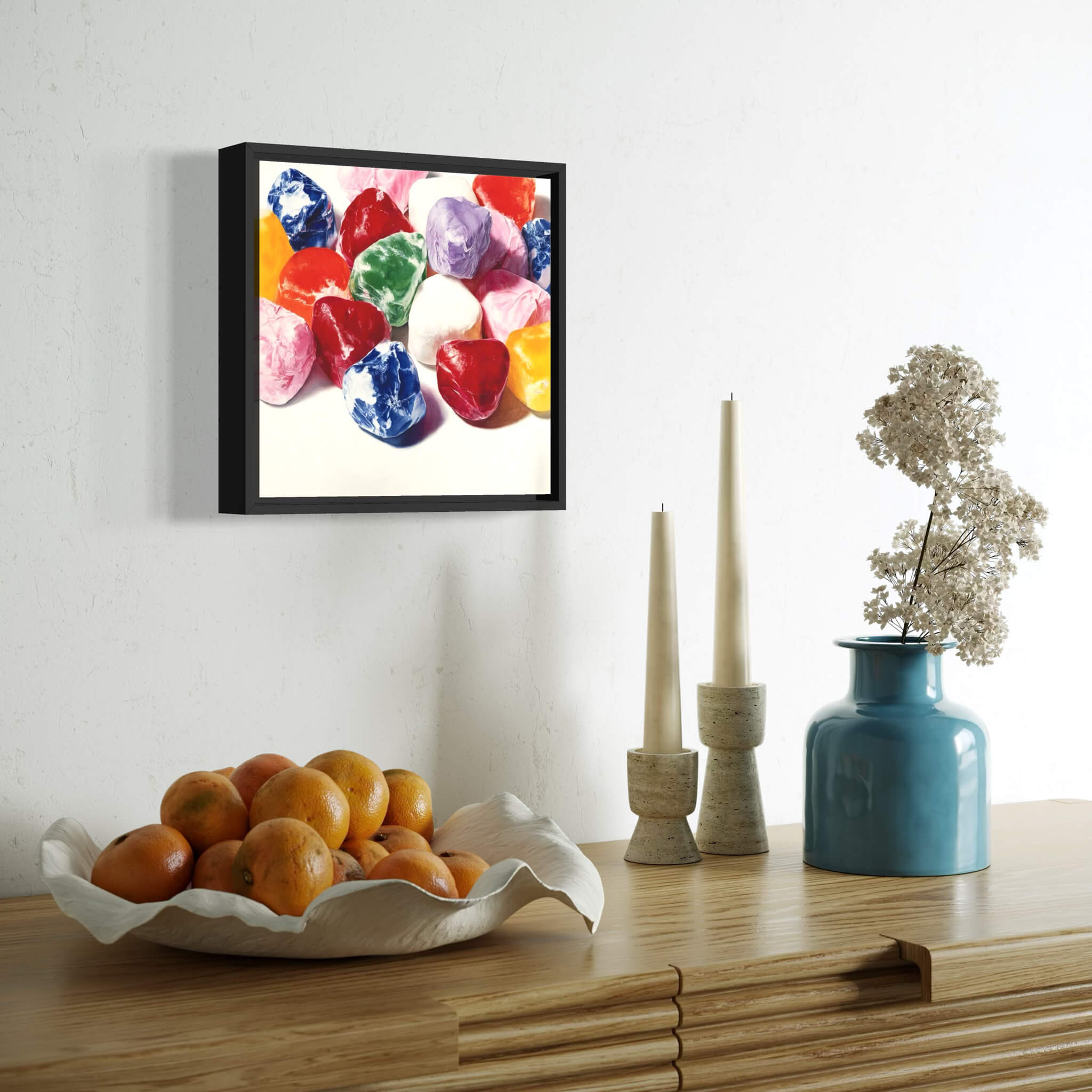 Decorative setup with a framed artwork, bowl of oranges, candles, and a vase on a wooden surface.