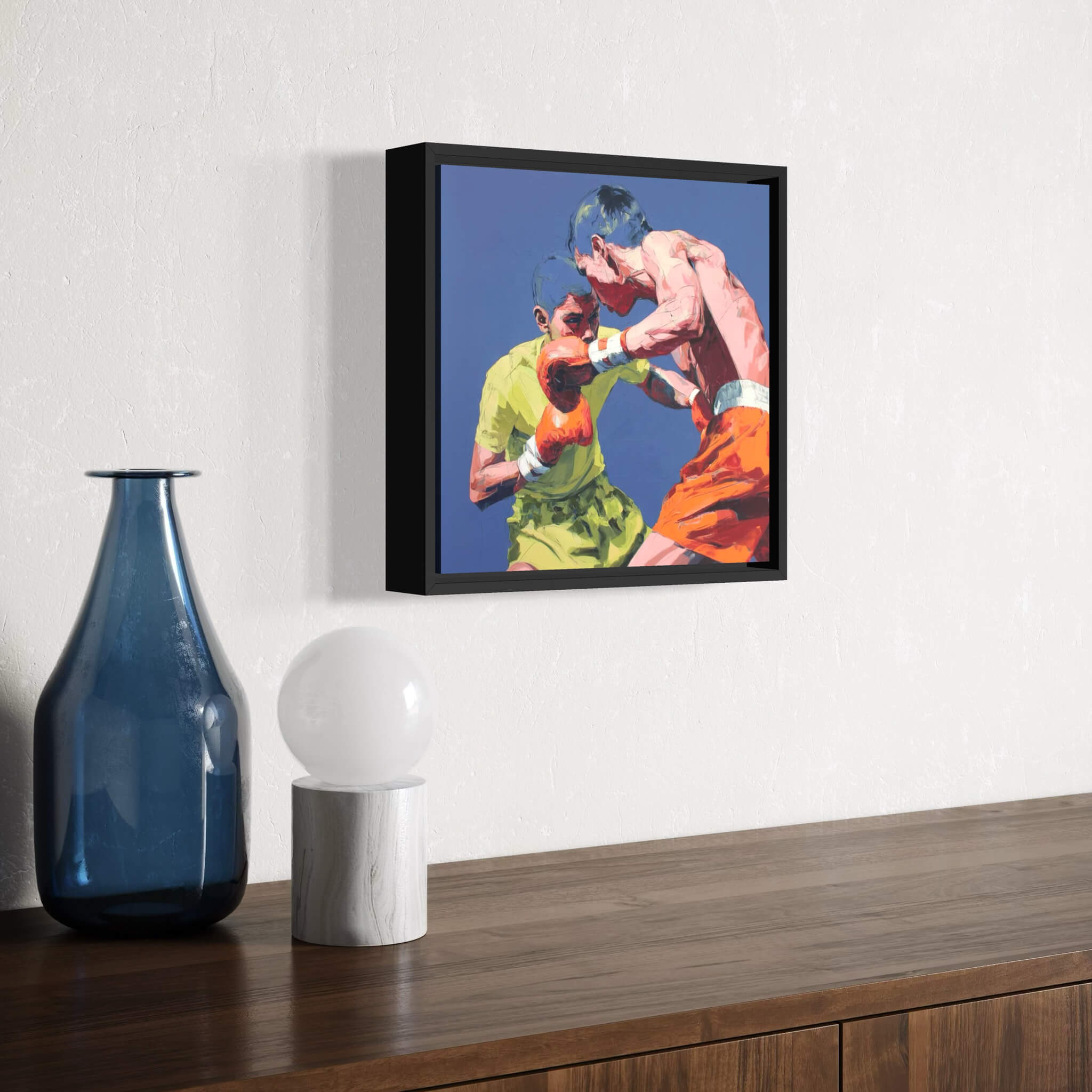 Framed artwork of a boxing match fine art oil painting on a wall above a wooden surface with decorative items.